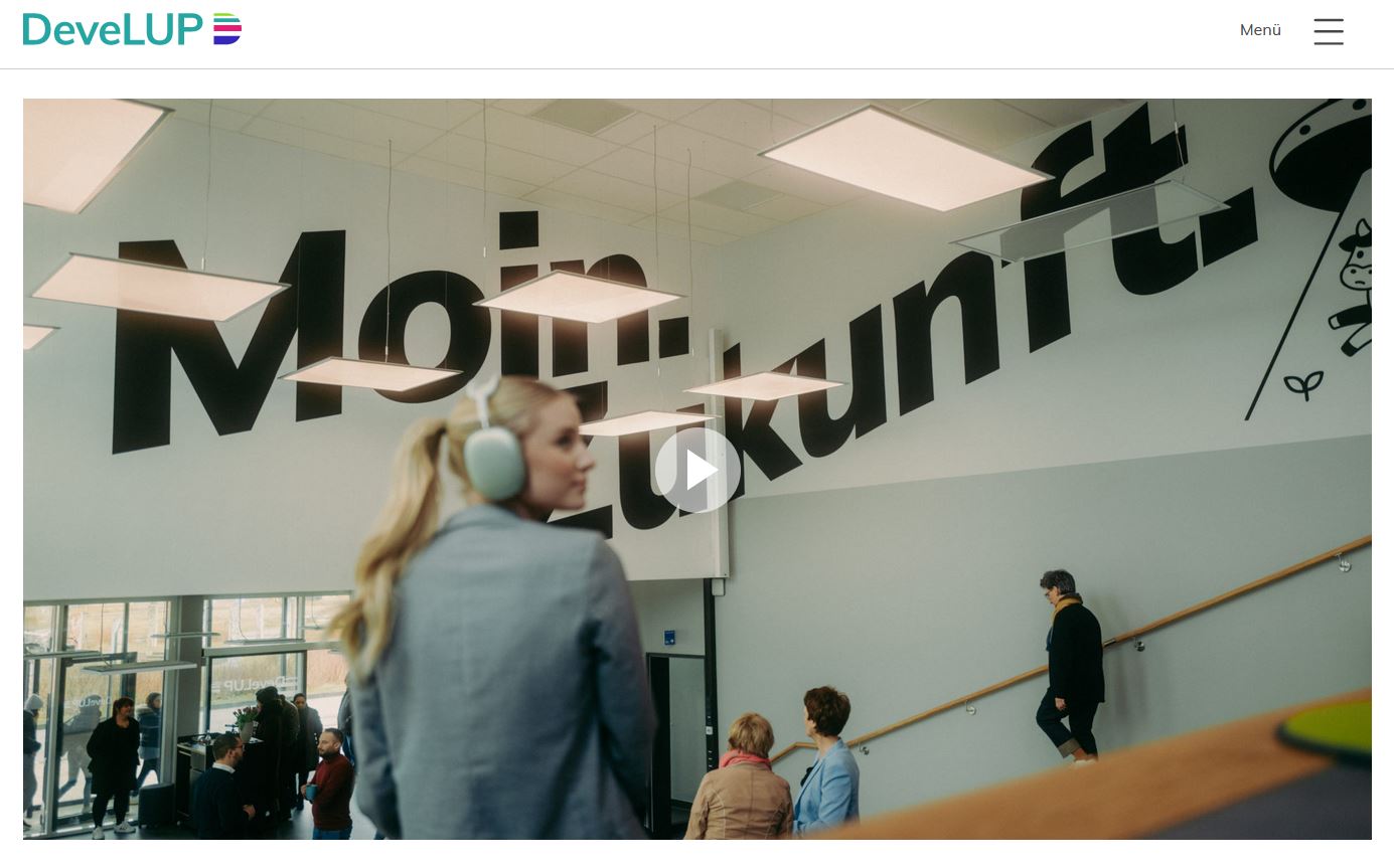 Foyer in einem Gründerzentrum mit Besuchern, schwebende, leuchtende LED-Paneele, an der Wand steht in großen schwarzen Buchstaben: "Moin Zukunft". Bild führt zu einer Websiete mit Imagefilm.
