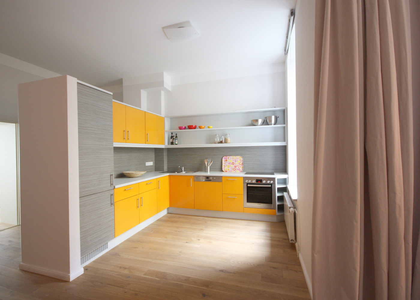 L-förmige Einbauküche mit orangen Fronten. Kühlschranktüren und Rückwandpaneel in strukturiertem Grau.