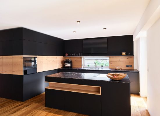 luxuriöse Designerküche in schwarz mit Holzelementen und Deckplatte in Marmor-Optik; Eicheparkett; horizontales Fensterband über der Spüle.
