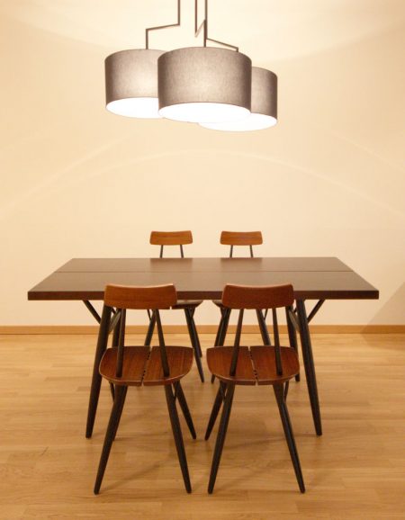 Ein schlichter Designer-Esstisch und vier passende Holzstühle in dunklen Tönen. Darüber eine schwarze Leuchte mit drei Lampenschirmen.