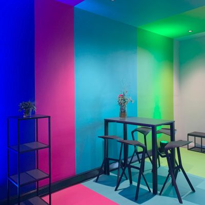 Ausstellungsraum mit farbigen Streifen in Dunkelblau, Pink, Cyan und Hellgrün, die über Wand, Boden und Decke gehen.