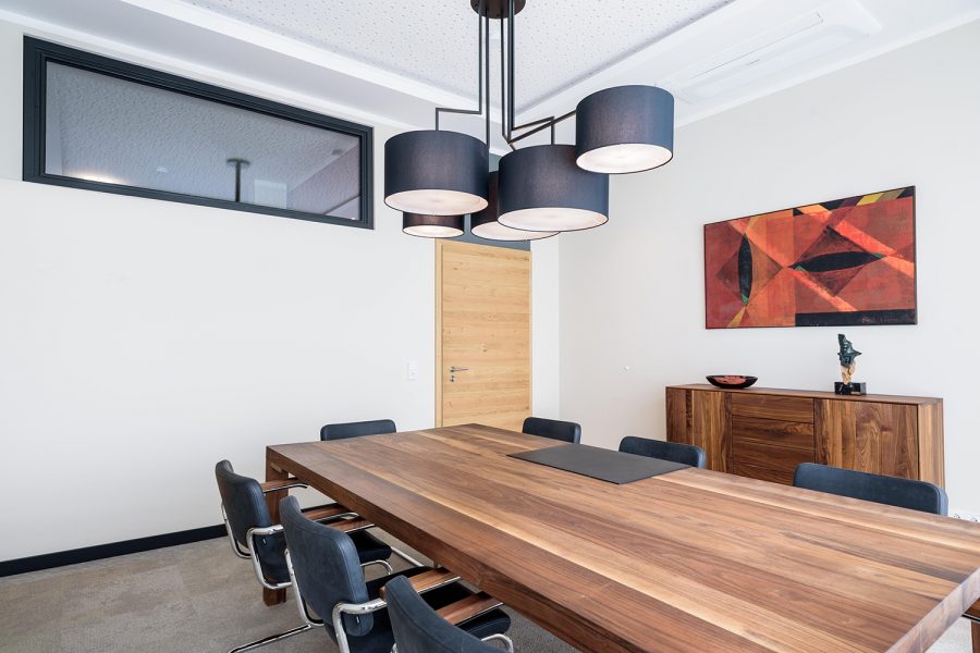 Konferenzraum mit Holzmöbeln in Nussbaum, schwarze Deckenleuchte von Zeitraum, Oberlicht mit schwarzem Rahmen, Gemälde in Rottönen, Teppichfliesen von Interface