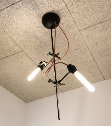 Eine Deckenleuchte als künstlerische Eigenkreation: An einem schwarzen Stab sind Lampenfassungen mit länglichen LED-Lampen mittels Klemmen fixiert.