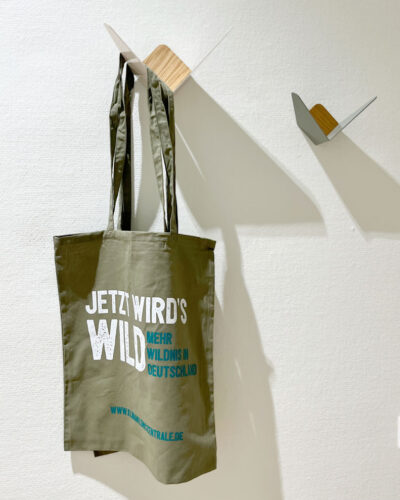 Ein Stoffbeutel mit der Aufschrift "Jetzt wird's wild" hängt an einem modernen Wandhaken.